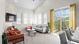 Living room with a stone fireplace, carpet floors, high vaulted ceiling, and ceiling fan