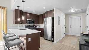 Kitchen featuring kitchen peninsula, a kitchen bar, light hardwood / wood-style flooring, stainless steel appliances, and decorative light fixtures