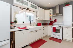 Kitchen with wall chimney range hood, white cabinetry, and white appliances