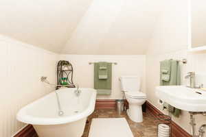 Bathroom featuring sink, a bath, vaulted ceiling, and toilet