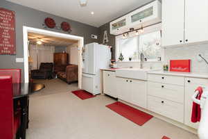 Kitchen featuring white cabinets, ceiling fan, backsplash, sink, and white refrigerator with ice dispenser