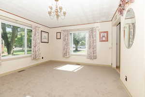 Carpeted empty room with crown molding and an inviting chandelier