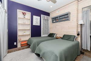 Bedroom with ceiling fan, wooden walls, and hardwood / wood-style floors