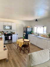 Kitchen with stainless steel appliances, sink, light wood-type flooring, white cabinetry, and a textured ceiling