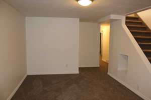 Empty room featuring dark carpet and a textured ceiling