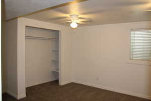 Unfurnished bedroom with dark colored carpet, a textured ceiling, a closet, and ceiling fan