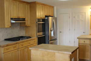 Kitchen with backsplash, appliances with stainless steel finishes, tile countertops, a textured ceiling, and a center island