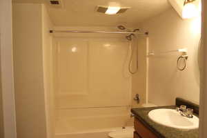 Full bathroom with vanity, a textured ceiling, toilet, and tub / shower combination