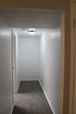 Hallway featuring dark colored carpet and a textured ceiling