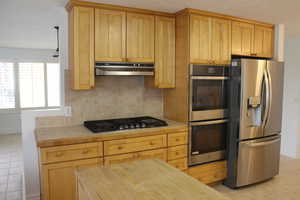 Kitchen featuring tile countertops, decorative backsplash, stainless steel appliances, and light tile patterned floors