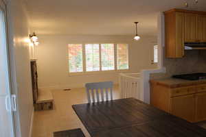 Kitchen with tile counters, light tile patterned flooring, pendant lighting, black gas stovetop, and tasteful backsplash