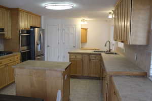 Kitchen with light brown cabinetry, sink, appliances with stainless steel finishes, a textured ceiling, and a center island