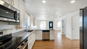 Kitchen featuring light stone countertops, white cabinetry, sink, stainless steel appliances, and light wood-type flooring