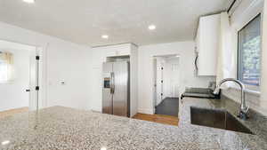 Kitchen featuring plenty of natural light, white cabinetry, sink, and stainless steel refrigerator with ice dispenser