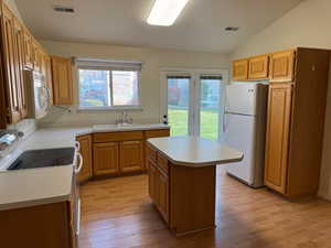 Kitchen featuring a center island, sink, light hardwood / wood-style flooring, vaulted ceiling, and white appliances