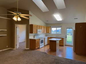 Kitchen featuring light wood-type flooring, white appliances, lofted ceiling with skylight, ceiling fan, and a center island