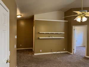 Carpeted spare room featuring vaulted ceiling and ceiling fan