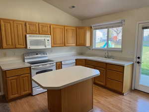 Kitchen with white appliances, vaulted ceiling, sink, light hardwood / wood-style flooring, and a kitchen island