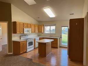 Kitchen featuring light wood-type flooring, white appliances, sink, a center island, and lofted ceiling