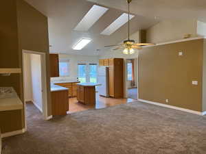 Kitchen with light carpet, lofted ceiling with skylight, sink, a center island, and white fridge