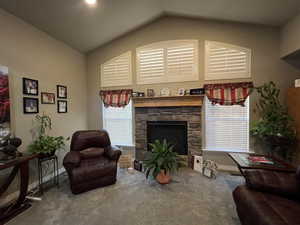 Carpeted living room with a wealth of natural light, vaulted ceiling, and a stone fireplace