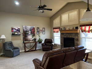 Carpeted living room with a fireplace, plenty of natural light, lofted ceiling, and ceiling fan