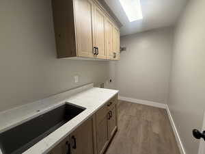 Laundry room featuring hookup for an electric dryer, sink, cabinets, and light wood-type flooring