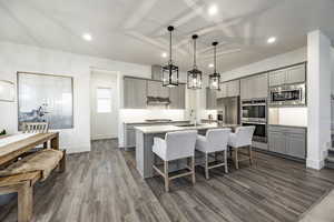 Kitchen with gray cabinetry, stainless steel appliances, a center island with sink, and hanging light fixtures