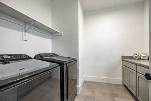 Laundry area featuring light tile patterned floors, separate washer and dryer, and cabinets