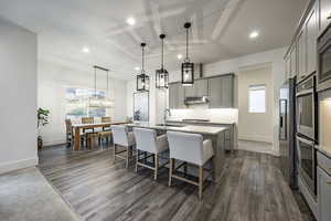 Kitchen with gray cabinetry, a healthy amount of sunlight, decorative light fixtures, and a center island with sink