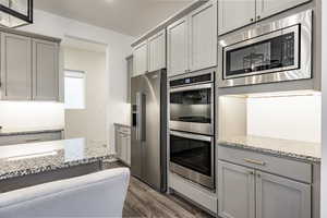 Kitchen with appliances with stainless steel finishes, light stone countertops, dark wood-type flooring, and gray cabinets