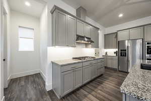 Kitchen with dark wood-type flooring, light stone counters, stainless steel appliances, and gray cabinetry