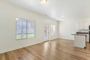 Unfurnished living room featuring sink, crown molding, light hardwood / wood-style floors, and plenty of natural light