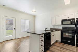 Kitchen featuring black appliances, white cabinetry, kitchen peninsula, and sink