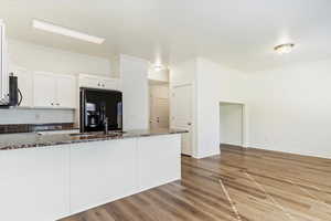 Kitchen with dark stone counters, black appliances, ornamental molding, white cabinetry, and light wood-type flooring