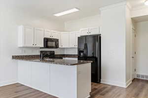 Kitchen featuring white cabinets, kitchen peninsula, black appliances, and dark stone counters