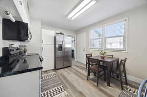 Kitchen featuring white cabinets, stainless steel refrigerator with ice dispenser, stove, and light wood-type flooring