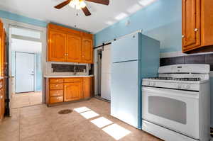 Kitchen featuring backsplash, a barn door, light tile patterned floors, white appliances, and ceiling fan