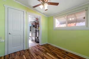 Unfurnished bedroom with lofted ceiling, dark hardwood / wood-style floors, crown molding, and ceiling fan