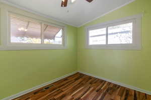 Empty room featuring dark wood-type flooring, ornamental molding, vaulted ceiling, and a healthy amount of sunlight