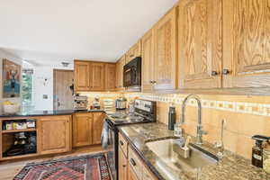 Kitchen featuring backsplash, dark stone countertops, sink, stainless steel electric range, and light wood-type flooring