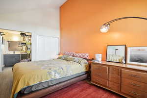 Bedroom with a closet, ensuite bathroom, high vaulted ceiling, and dark colored carpet