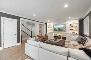 Living room with light hardwood / wood-style floors, crown molding, and built in features