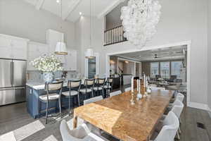 Dining space featuring dark wood-type flooring, a towering ceiling, ceiling fan with notable chandelier, and beam ceiling