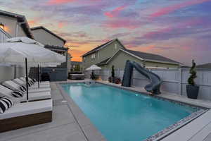 Pool at dusk featuring a water slide, a patio, and a jacuzzi