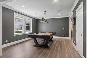 Game room with a textured ceiling, pool table, hardwood / wood-style floors, and crown molding