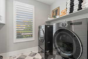 Clothes washing area featuring separate washer and dryer, cabinets, and light tile patterned floors