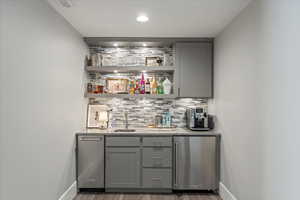 Bar featuring light stone countertops, backsplash, gray cabinetry, and stainless steel fridge