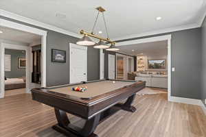 Rec room with billiards, a textured ceiling, light wood-type flooring, and ornamental molding