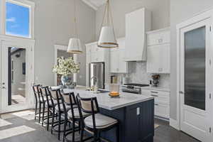 Kitchen featuring stainless steel appliances, white cabinetry, dark hardwood / wood-style flooring, hanging light fixtures, and an island with sink